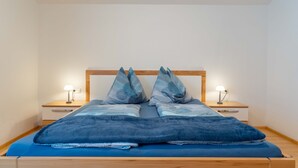 Uma cama com cabeceira de madeira, duas mesas de cabeceira com luminárias e um cobreleira azul.