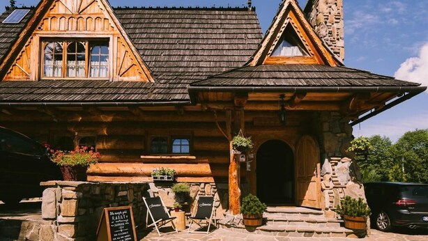 A rustic wooden building with a stone chimney, a wooden door, and a signboard. - Javorina Residence (Zakopane)
