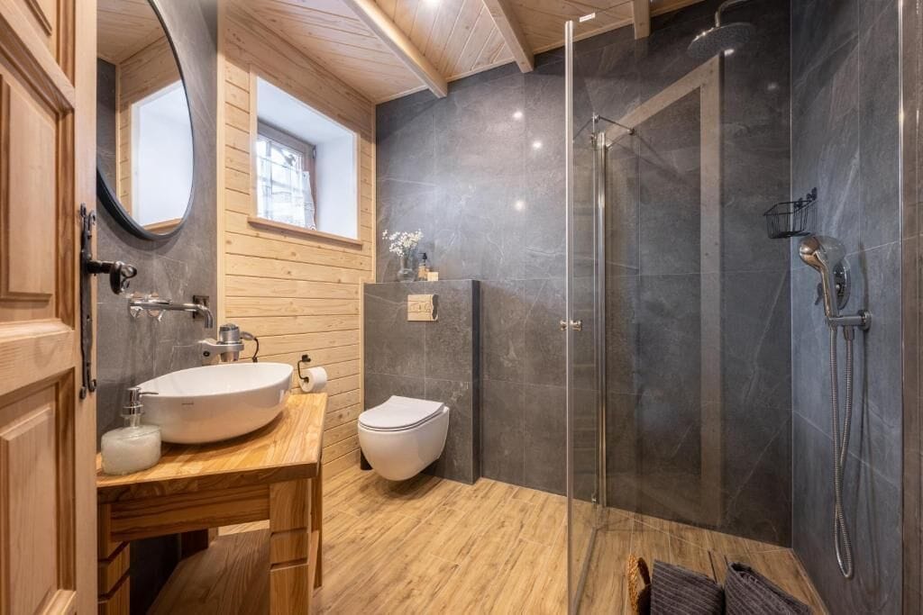 A bathroom with a wooden vanity, a white sink, a toilet, and a glass-enclosed shower.