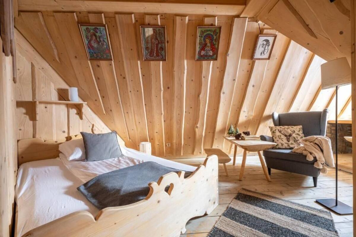 Una habitación de madera con una cama, una silla, una mesita y cuadros en la pared.