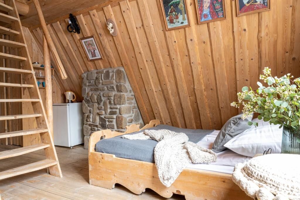 A wooden room with a bed, a stone wall, a ladder, and a small white appliance.