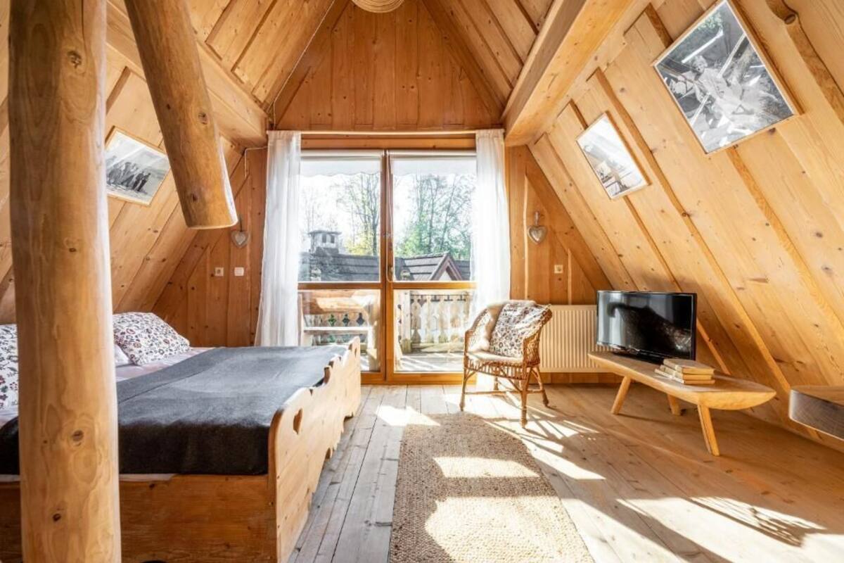Un dormitorio de cabaña de madera con una cama, una silla, un televisor y un ventanal grande.