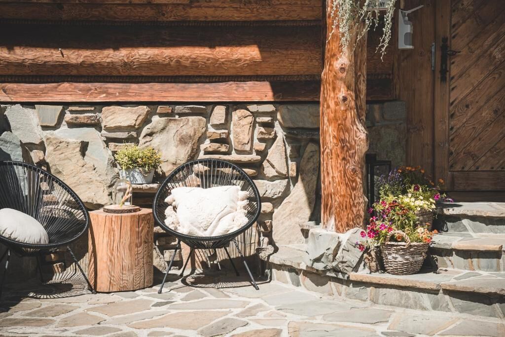A rustic outdoor seating area with stone walls, wooden beams, and wicker chairs.