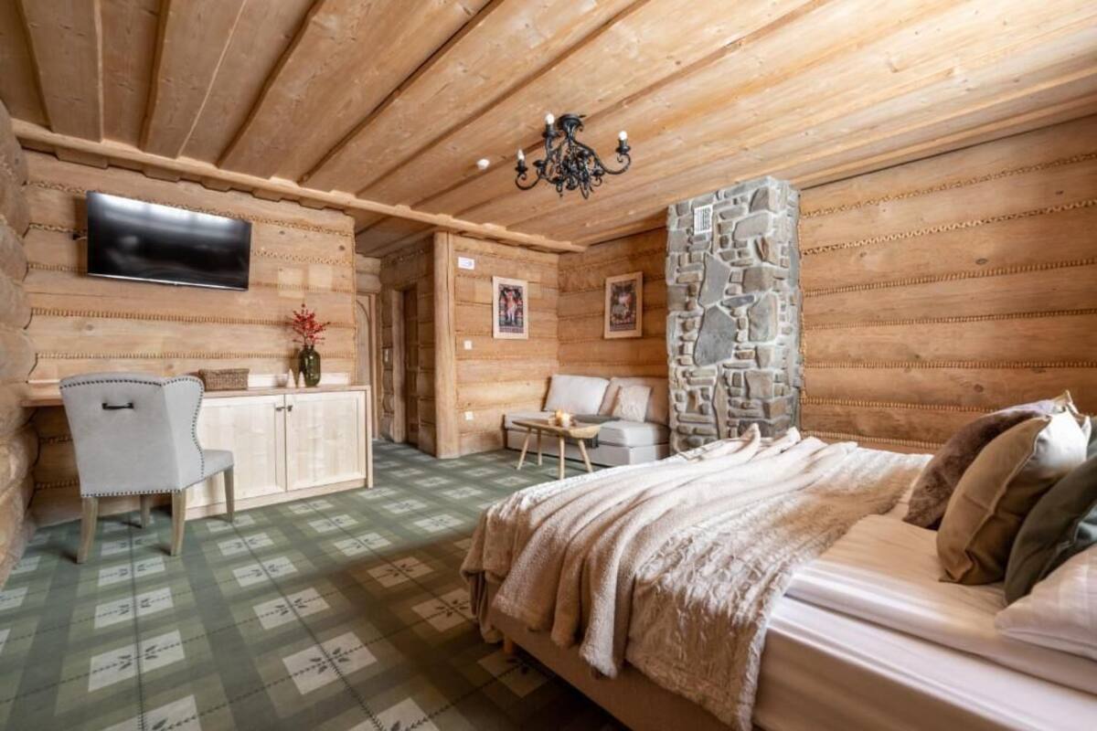 Habitación de cabaña de troncos con cama, escritorio, silla, televisor y pared de piedra.