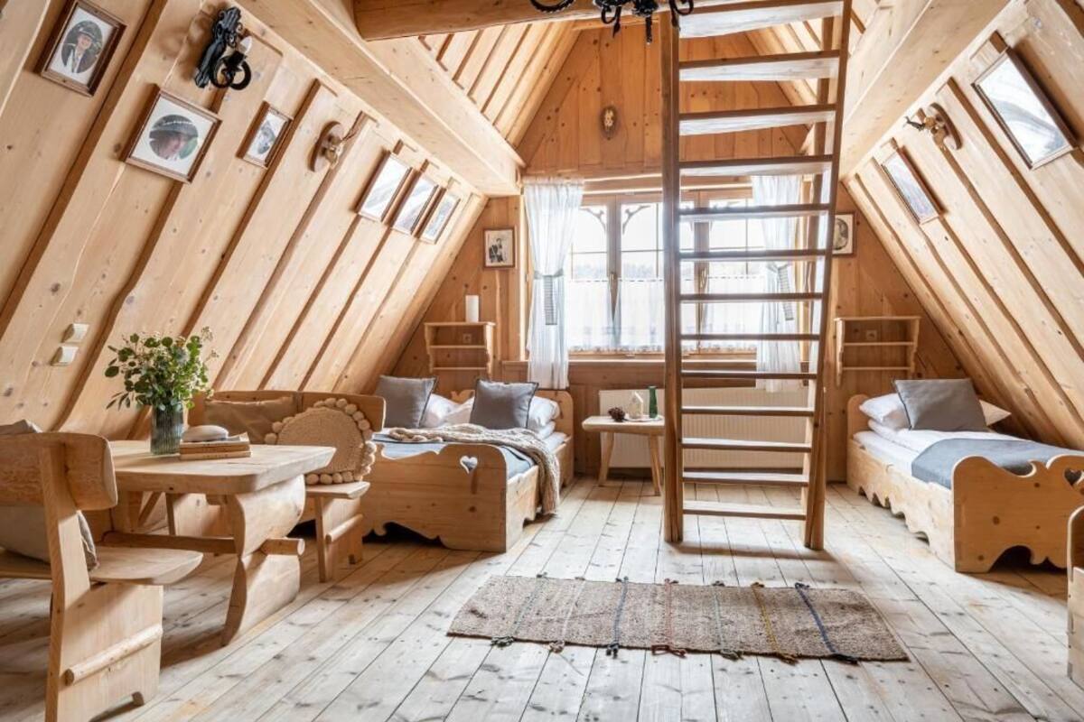Una habitación de ático con piso de madera, una cama alta, una mesa de comedor y una escalera.