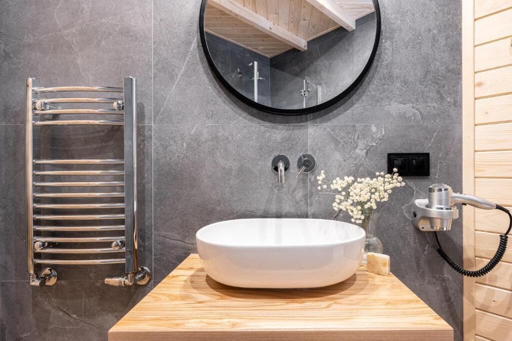 Un baño con un espejo redondo, un lavamanos blanco, un perchero y un cabezal de ducha manual.