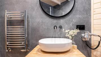 Un baño con un espejo redondo, un lavamanos blanco, un perchero y un cabezal de ducha manual.