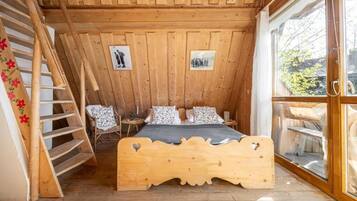 Un dormitorio de cabaña de madera con una cama, una silla, una escalera y un ventanal.