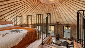 A room with a wooden ceiling, a bed, a fireplace, and a view through a window. - Mojave Yurt Featured in Rolling Stone, Stargaze (San Bernardino County)