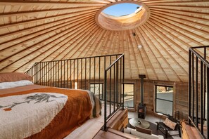Ein Zimmer mit Holzbalkendecke, einem Bett, einem Kamin und Blick durch ein Fenster.