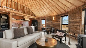 A modern interior with a wooden ceiling, a sofa, a round coffee table, a dining area, and a kitchen. - Mojave Yurt Featured in Rolling Stone, Stargaze (San Bernardino County)