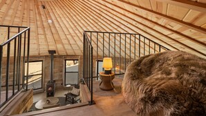 A wooden interior with a high ceiling, a fireplace, a round table, and a fur-covered ottoman. - Mojave Yurt Featured in Rolling Stone, Stargaze (San Bernardino County)