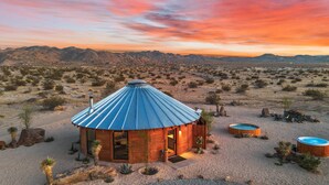 A wooden yurt with a blue roof, surrounded by desert vegetation and mountains in the background. - Mojave Yurt Featured in Rolling Stone, Stargaze (San Bernardino County)