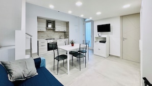 Een moderne keuken met witte kasten, een eettafel met stoelen, een aan de muur bevestigde televisie en een trap naar een ander niveau.