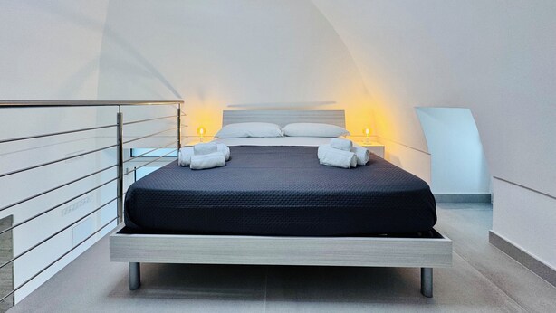 Een moderne slaapkamer met een bed, nachtlampjes en een bijzonder plafondontwerp.