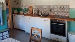 Uma cozinha com vigas de madeira, bancada branca, pia, armários e forno.