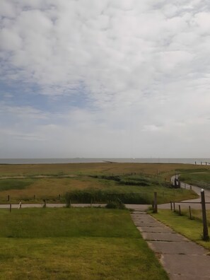 A pathway leading to a grassy area with a view of the sea and distant hills. - Holiday Home 'Ferienhaus Petersen' with Sea View, Shared Terrace and Wi-Fi (Langeneß)