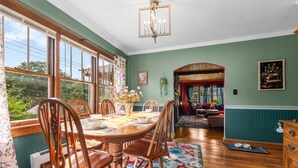 A dining area with a wooden table and chairs, a chandelier, and a view through large windows. - New! Hot Tub, Sauna, Arcade, cozy cottage - walk to everything! Great location! (Fayetteville)