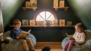 Two children reading books in a room with a sloped ceiling, a wooden floor, and a large window. - New! Hot Tub, Sauna, Arcade, cozy cottage - walk to everything! Great location! (Fayetteville)