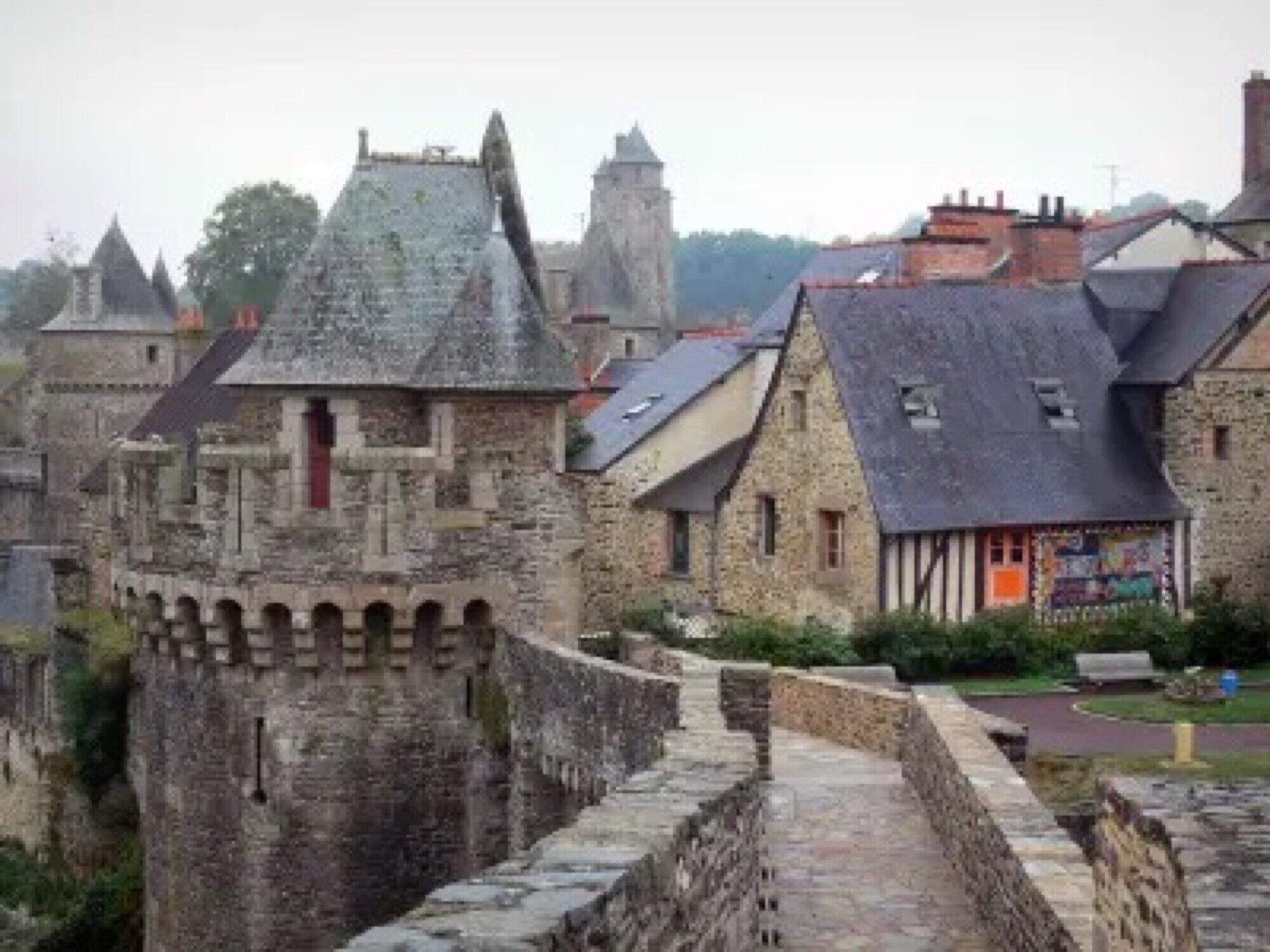 A historic stone castle with a fortified wall, traditional timber-framed buildings, and a paved pathway.