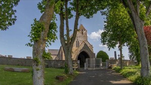 Una iglesia con una entrada de arco apuntado, rodeada de árboles y un muro de piedra.