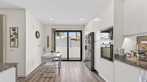 Een moderne keuken met witte kastjes, een eettafel met stoelen, een koelkast en een uitzicht door een glazen deur.