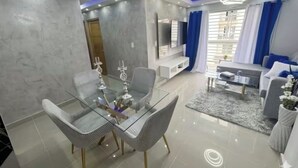A modern living room with a glass dining table, grey sofas, and a TV.