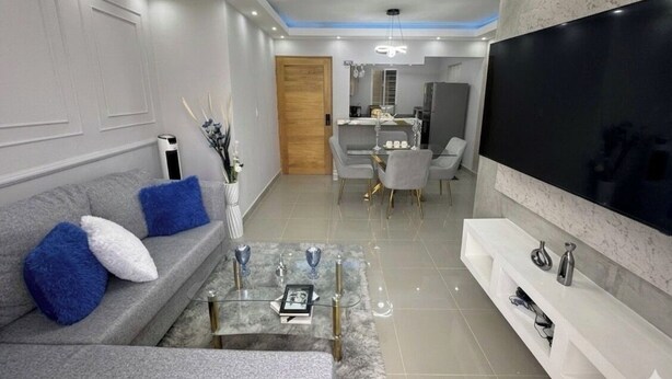 A modern living room with a sofa, coffee table, TV, and dining area.