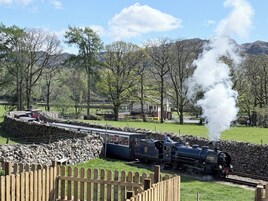Una locomotora de vapor sobre rieles, con un muro de piedra y una valla de madera al frente.