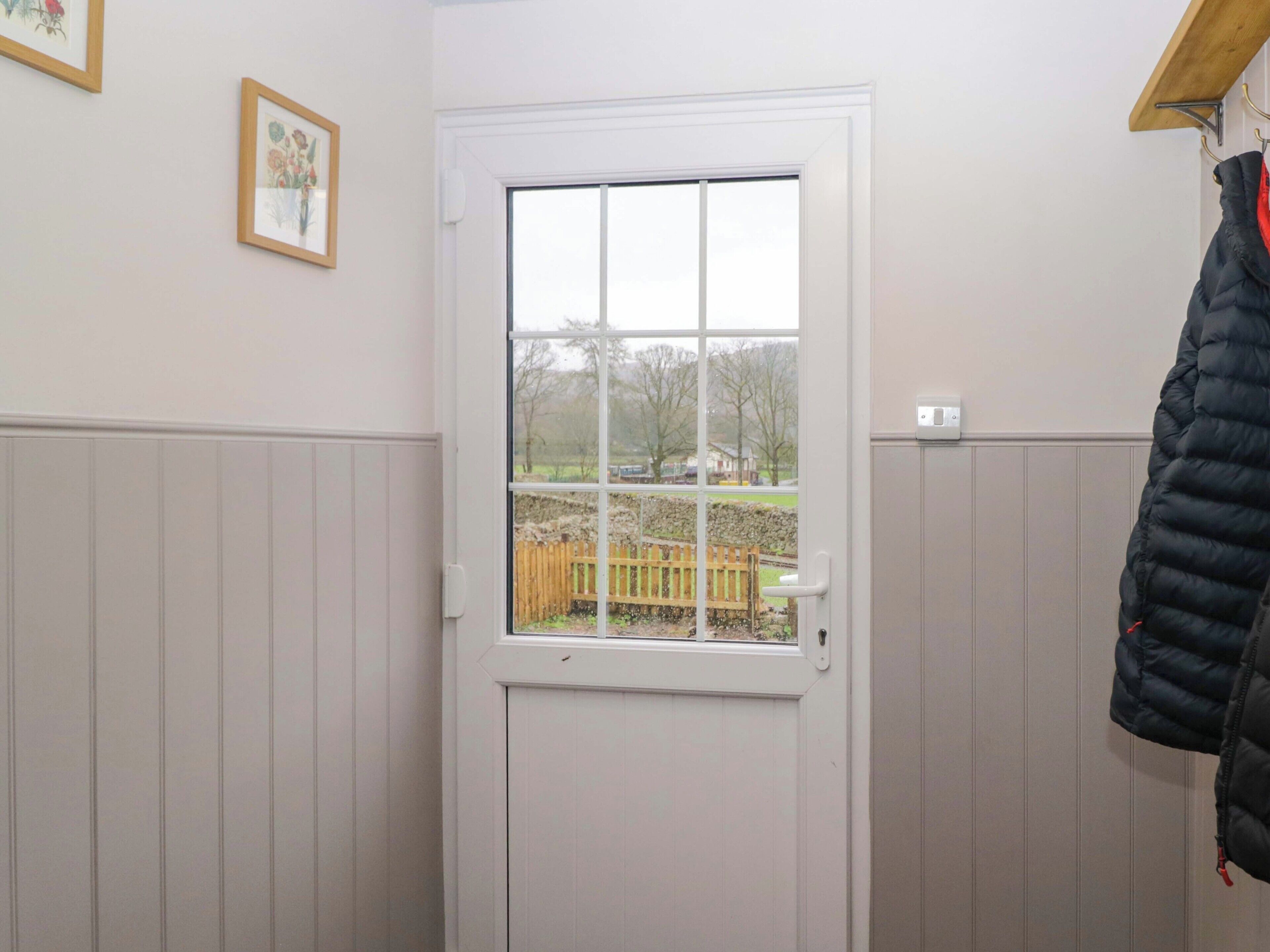 Una habitación con una puerta blanca, una ventana y un banco de madera en el exterior, además de un perchero.