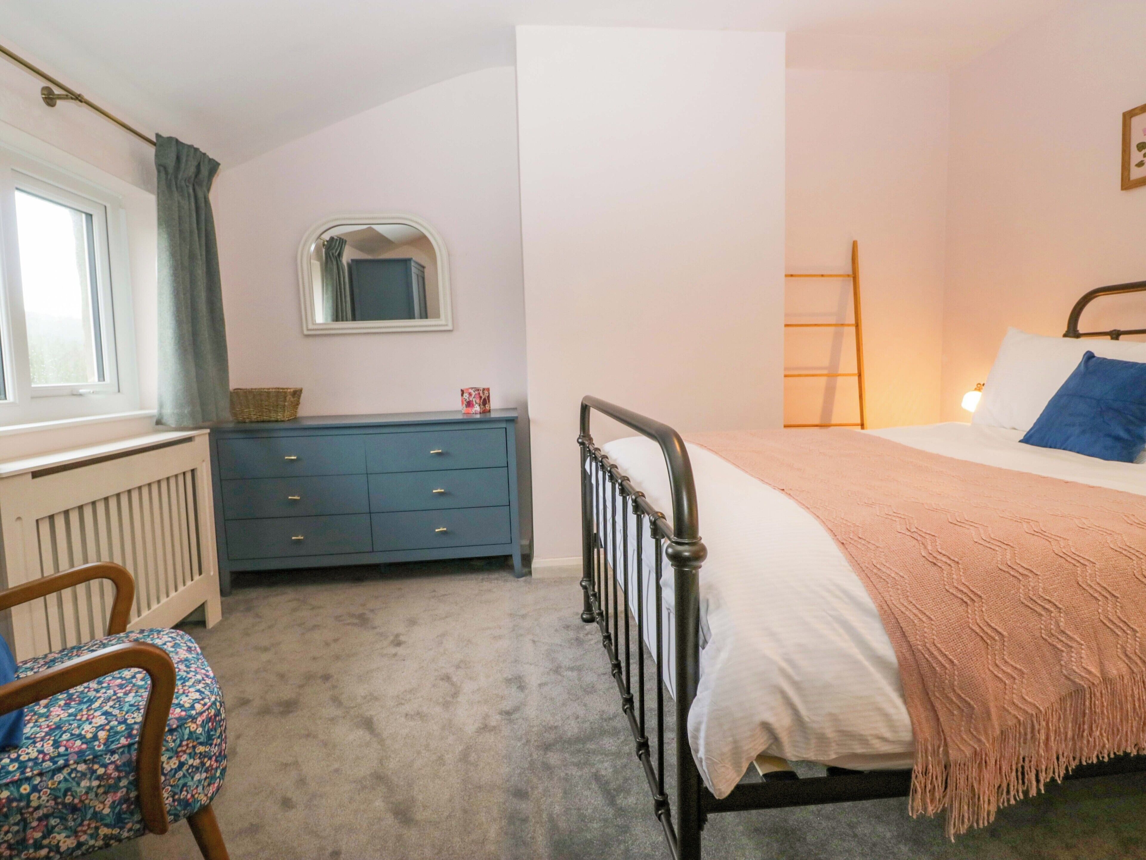 A bedroom with a bed, a dresser, a chair, a radiator, a window with curtains, and a mirror on the wall.