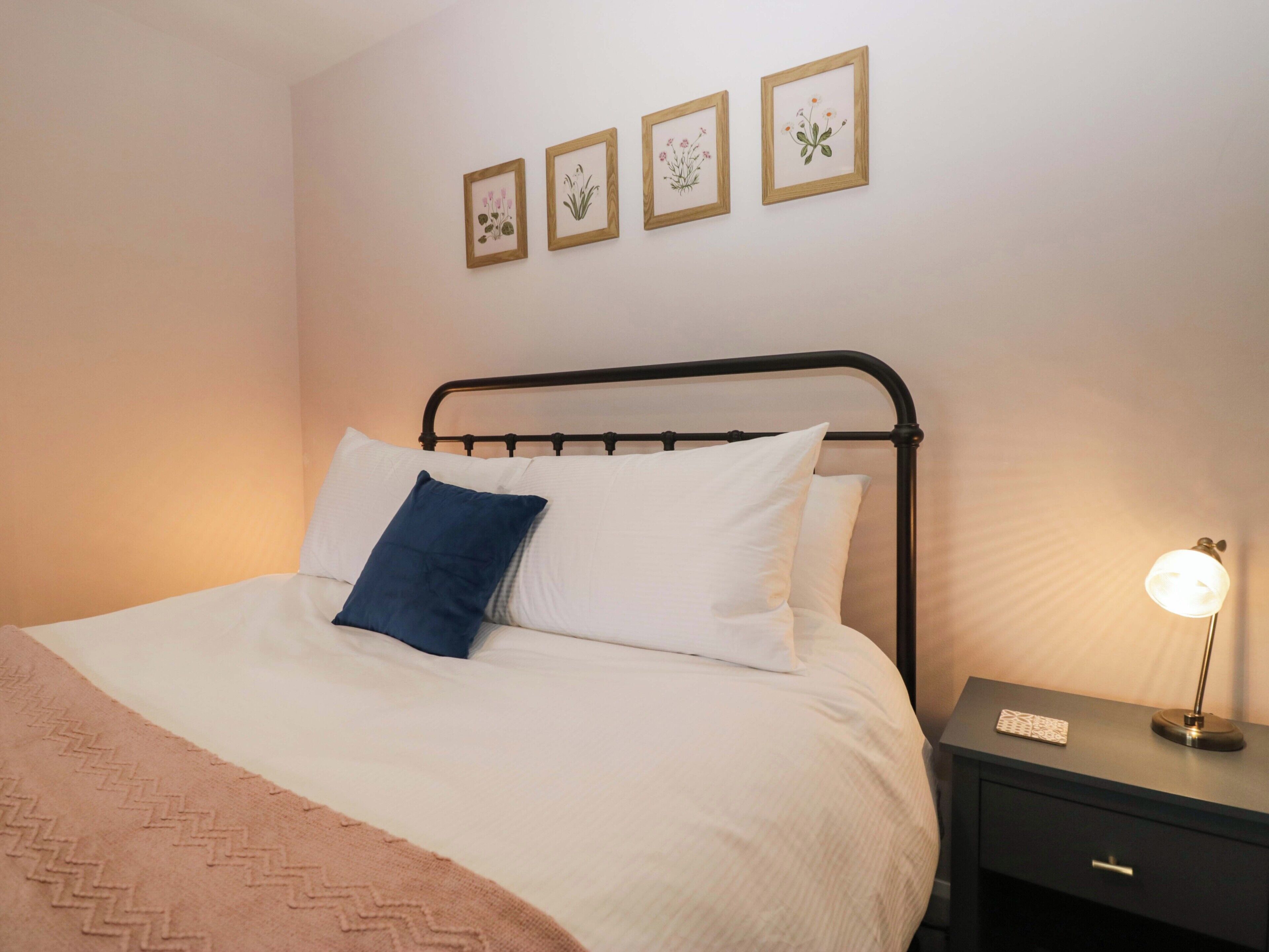 A neatly made bed with white and blue bedding, a black metal headboard, and a bedside table with a lamp.