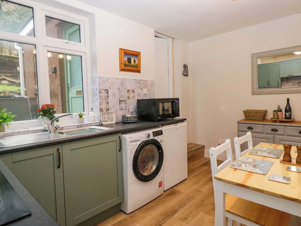 A compact kitchen with a washing machine, a microwave, and a dining area with a table and chairs. - Dakota (Holmrook)