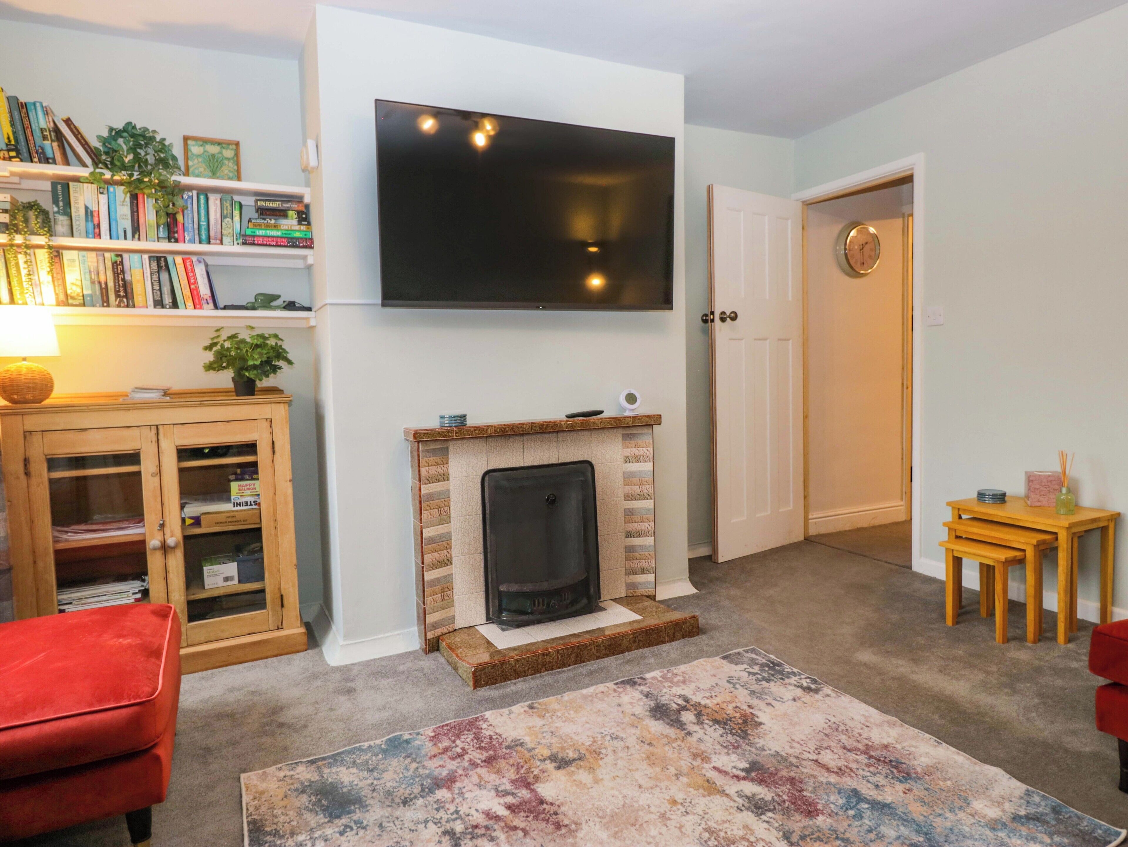 Een woonkamer met een open haard, een flatscreen-televisie, een boekenkast en een rode stoel.