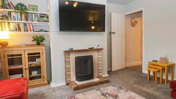 Een woonkamer met een open haard, een flatscreen-televisie, een boekenkast en een rode stoel.