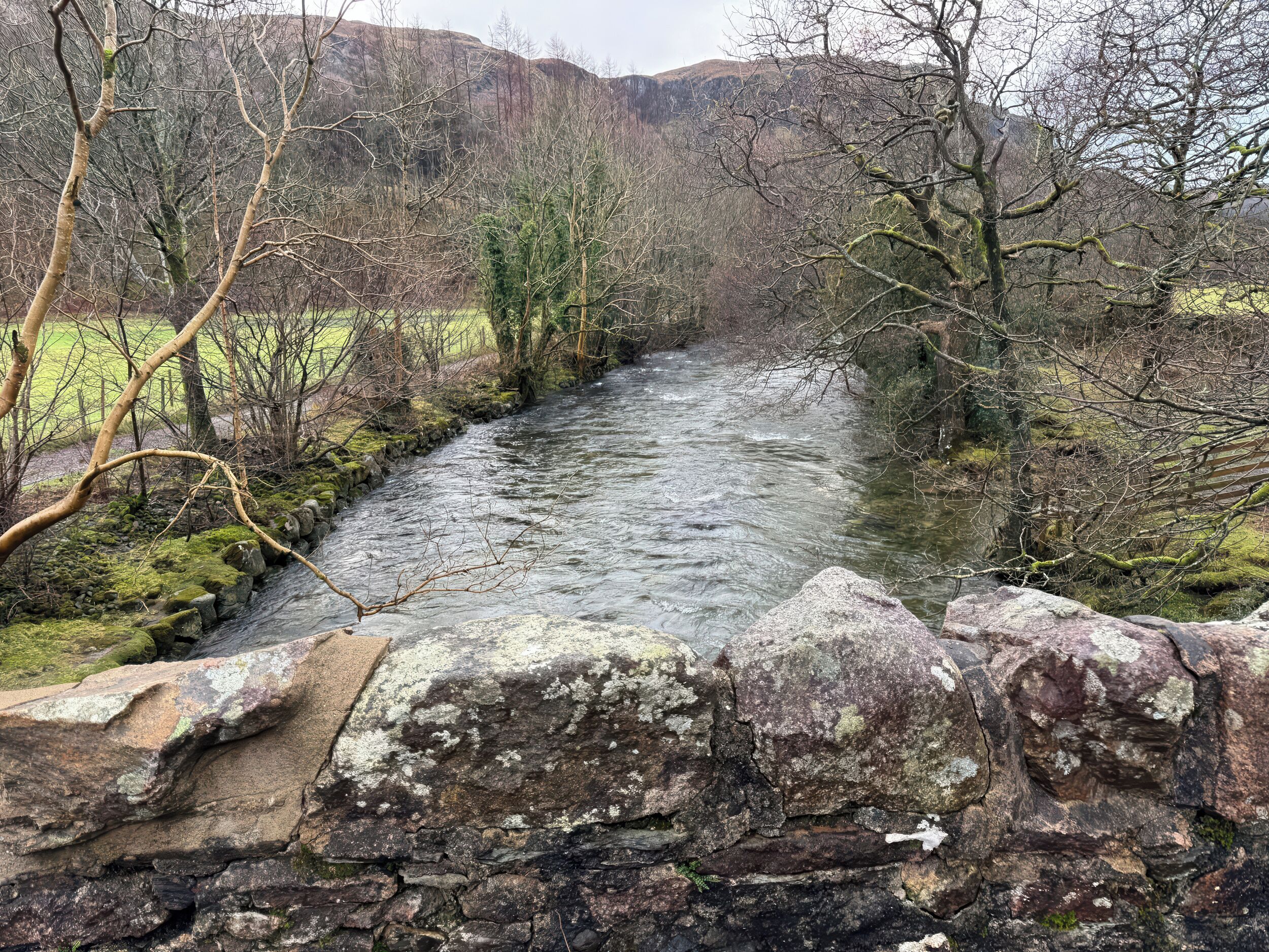 Un río serpentea por un valle con muros de piedra y árboles.