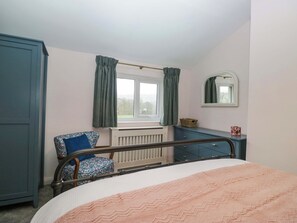 Um quarto com cama, cadeira, cômoda, radiador e janela com cortinas.