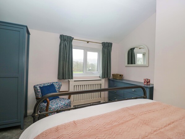 A bedroom with a bed, a chair, a dresser, a radiator, and a window with curtains.