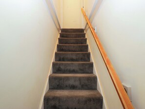 A carpeted staircase with a wooden handrail, white walls, and a white door at the top. - Dakota (Holmrook)