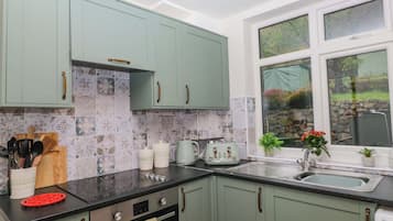 A kitchen with teal cabinets, a black countertop, and a window with a view of greenery.