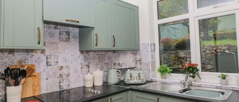 A kitchen with teal cabinets, a black countertop, and a window with a view of greenery.