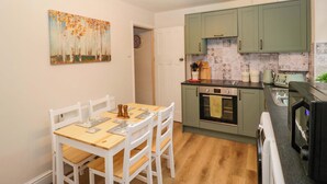 A compact kitchen with a dining table, chairs, a clock, and a painting on the wall. - Dakota (Holmrook)