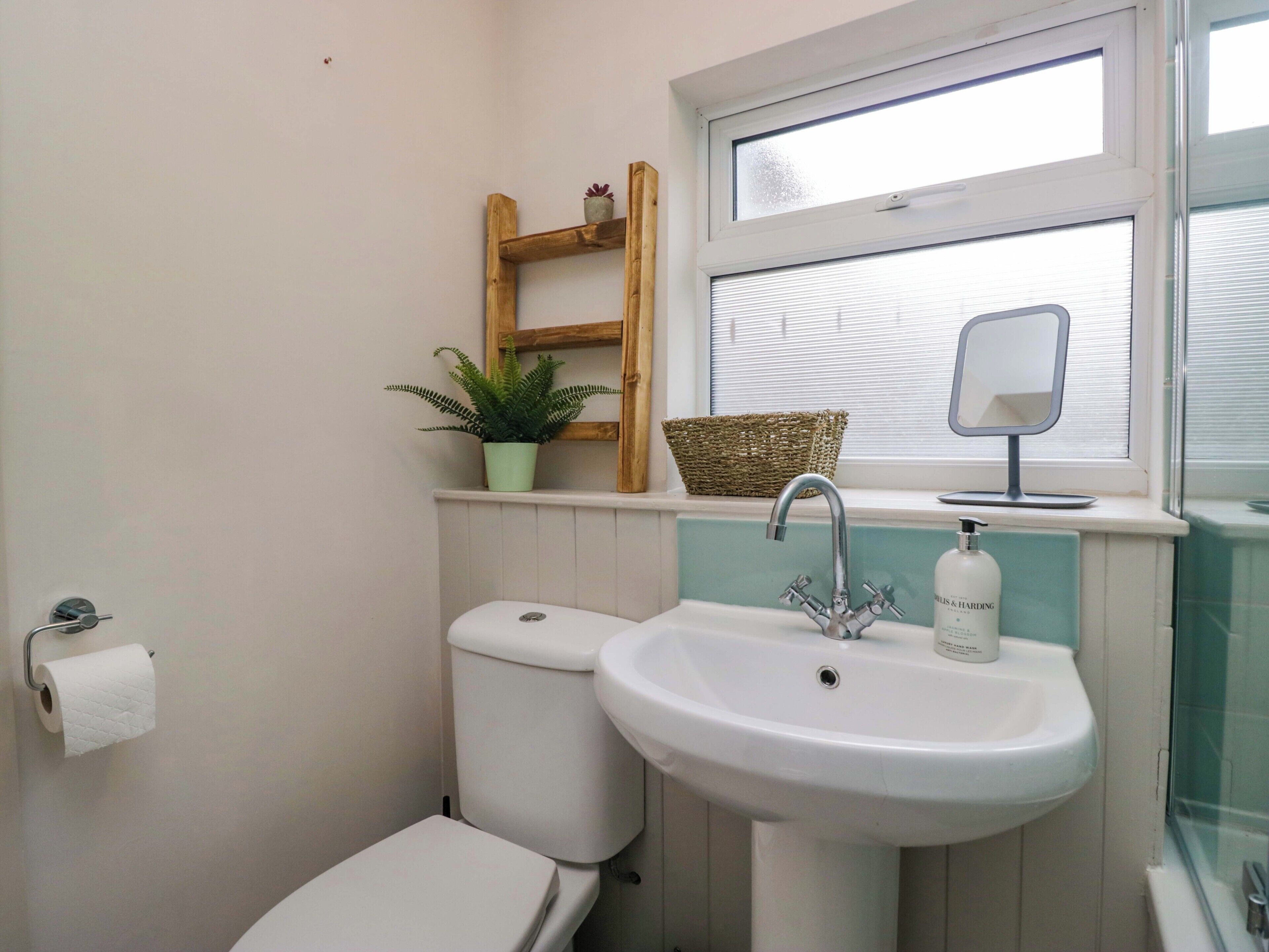 Un baño con inodoro, lavamanos, ventana, espejo, planta en maceta y estante de madera.