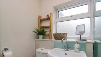 Un baño con inodoro, lavamanos, ventana, espejo, planta en maceta y estante de madera.