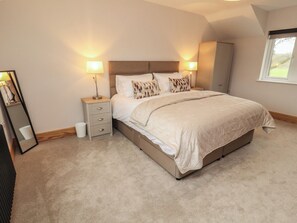 A bedroom with a bed, bedside lamps, a nightstand, a mirror, and a window. - The Gate House Annexe (Cockermouth)
