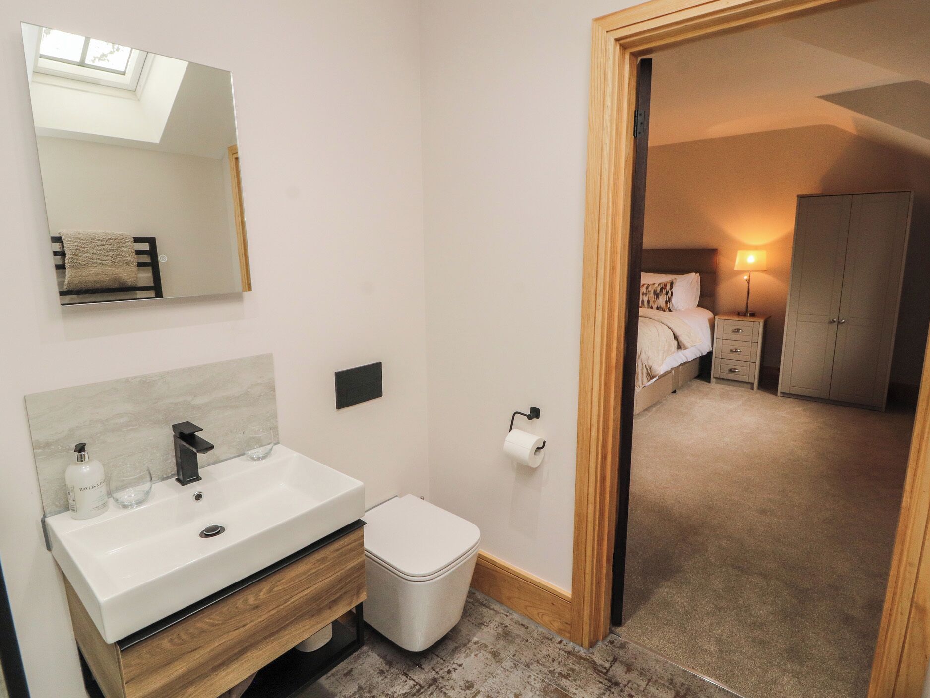 A bathroom with a sink, mirror, toilet, and a small trash bin.