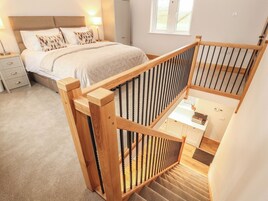 A bedroom with a bed, bedside table, lamp, and a wooden staircase railing.