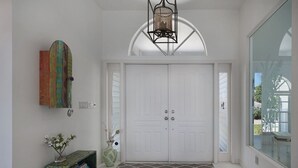 A hallway with a white door, a decorative light fixture, a vase with flowers, and a bookshelf. - Villa Southern Living, dreamy waterfront vacation home in Cape Coral (Cape Coral)