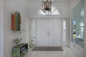 A hallway with a white door, a decorative light fixture, a vase with flowers, and a bookshelf. - Villa Southern Living, dreamy waterfront vacation home in Cape Coral (Cape Coral)