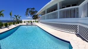A swimming pool with a view of the ocean, lounge chairs, and a white building with a balcony. - Villa Southern Living, dreamy waterfront vacation home in Cape Coral (Cape Coral)